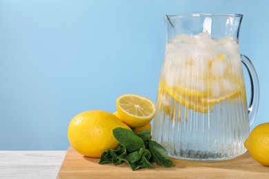 Freshly made lemonade with mint in jug on white wooden table against light blue background, space for text