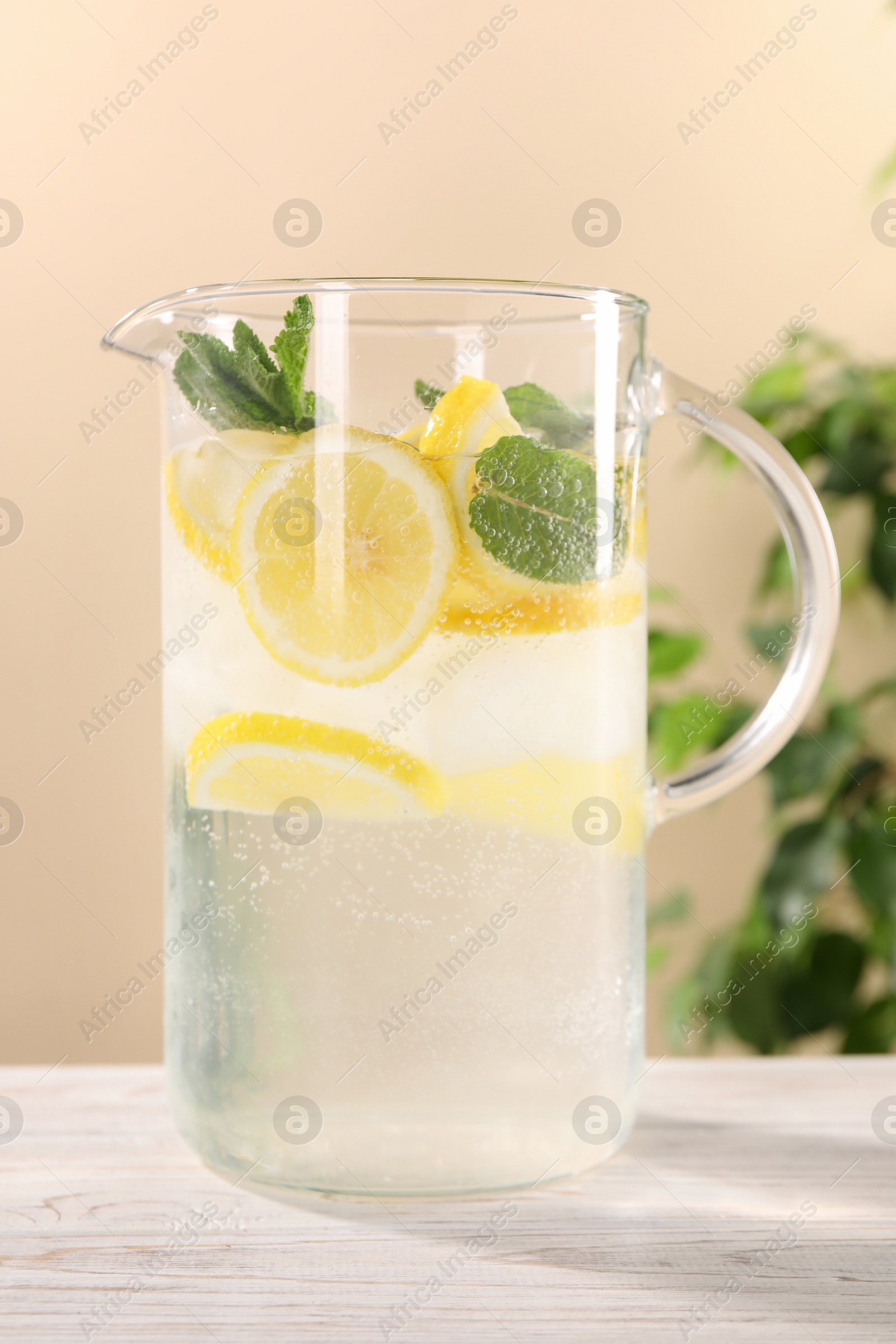 Photo of Freshly made lemonade with mint in jug on white wooden table against beige background