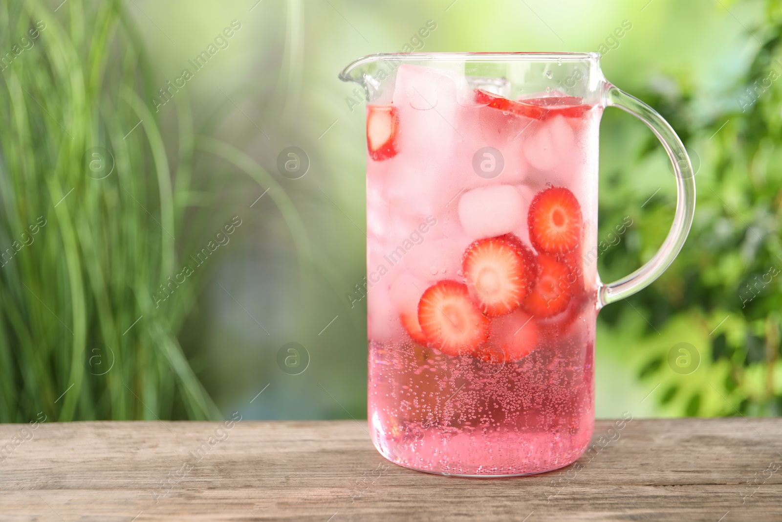 Photo of Freshly made strawberry lemonade in jug on wooden table outdoors, space for text