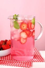 Freshly made strawberry lemonade with mint in jug on white wooden table against pink background