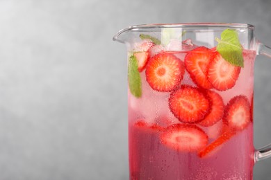 Photo of Freshly made strawberry lemonade with mint in jug and glass on grey background, closeup. Space for text