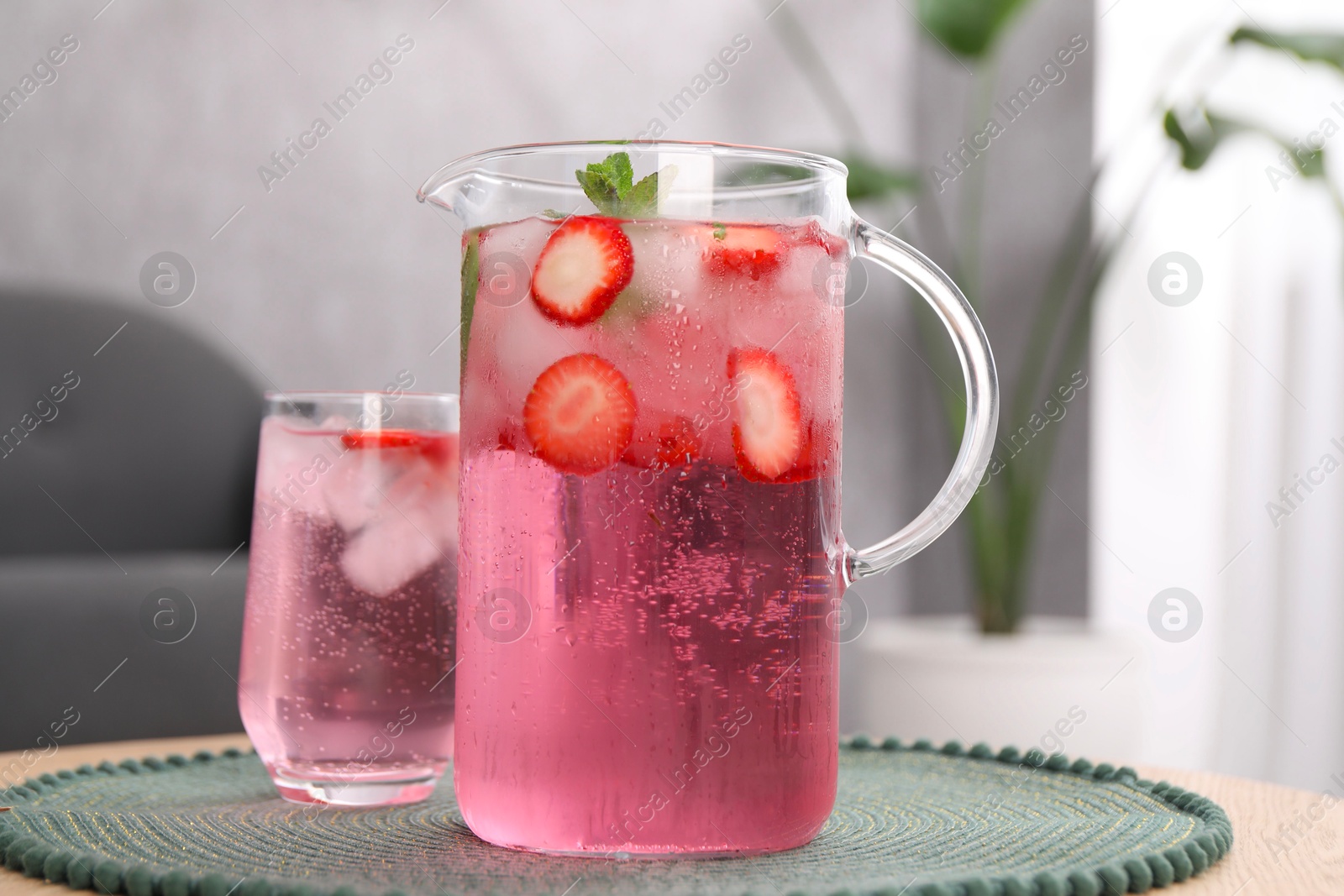 Photo of Freshly made strawberry lemonade with mint in jug and glass on wooden table indoors