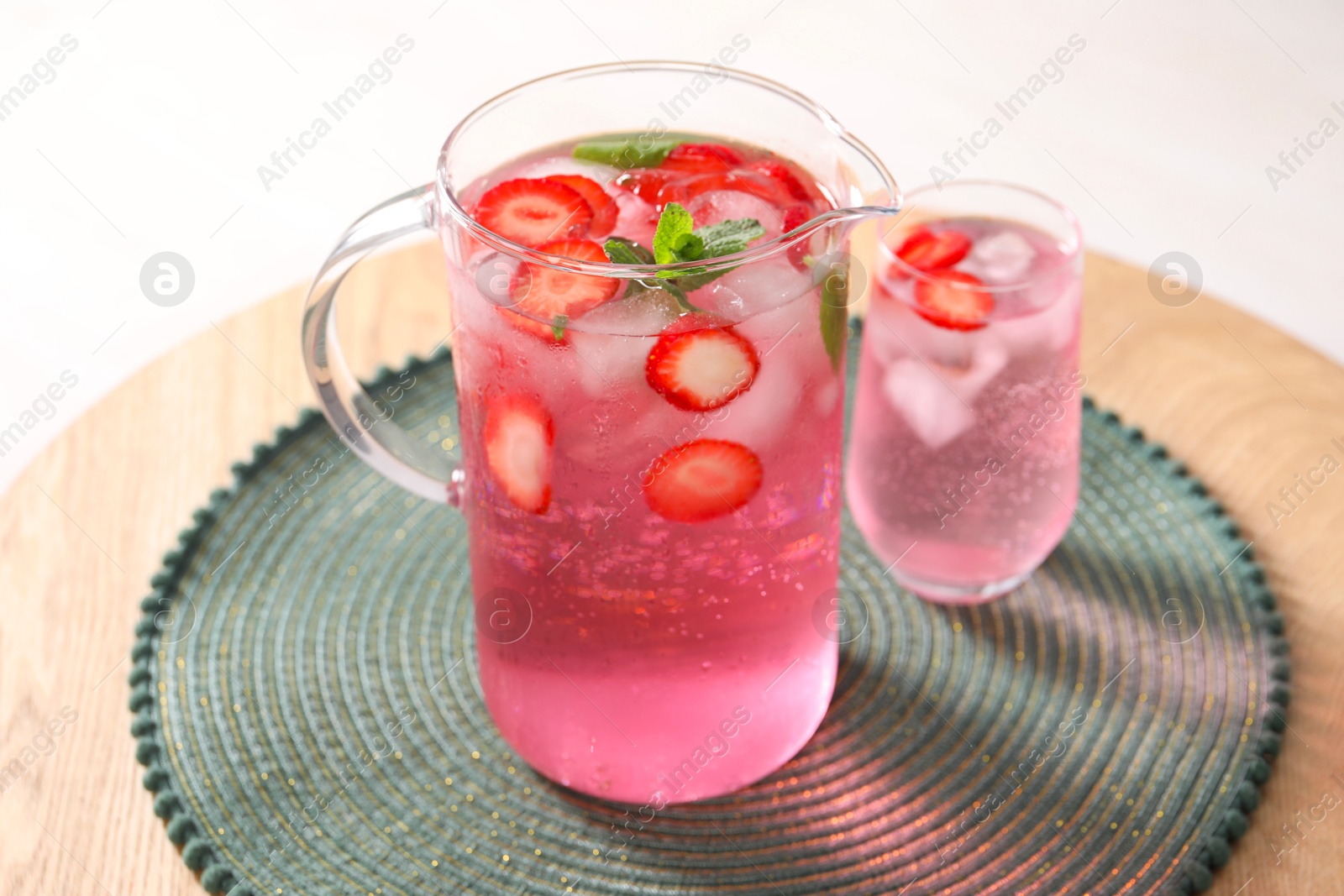 Photo of Freshly made strawberry lemonade with mint in jug and glass on wooden table