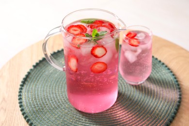 Photo of Freshly made strawberry lemonade with mint in jug and glass on wooden table