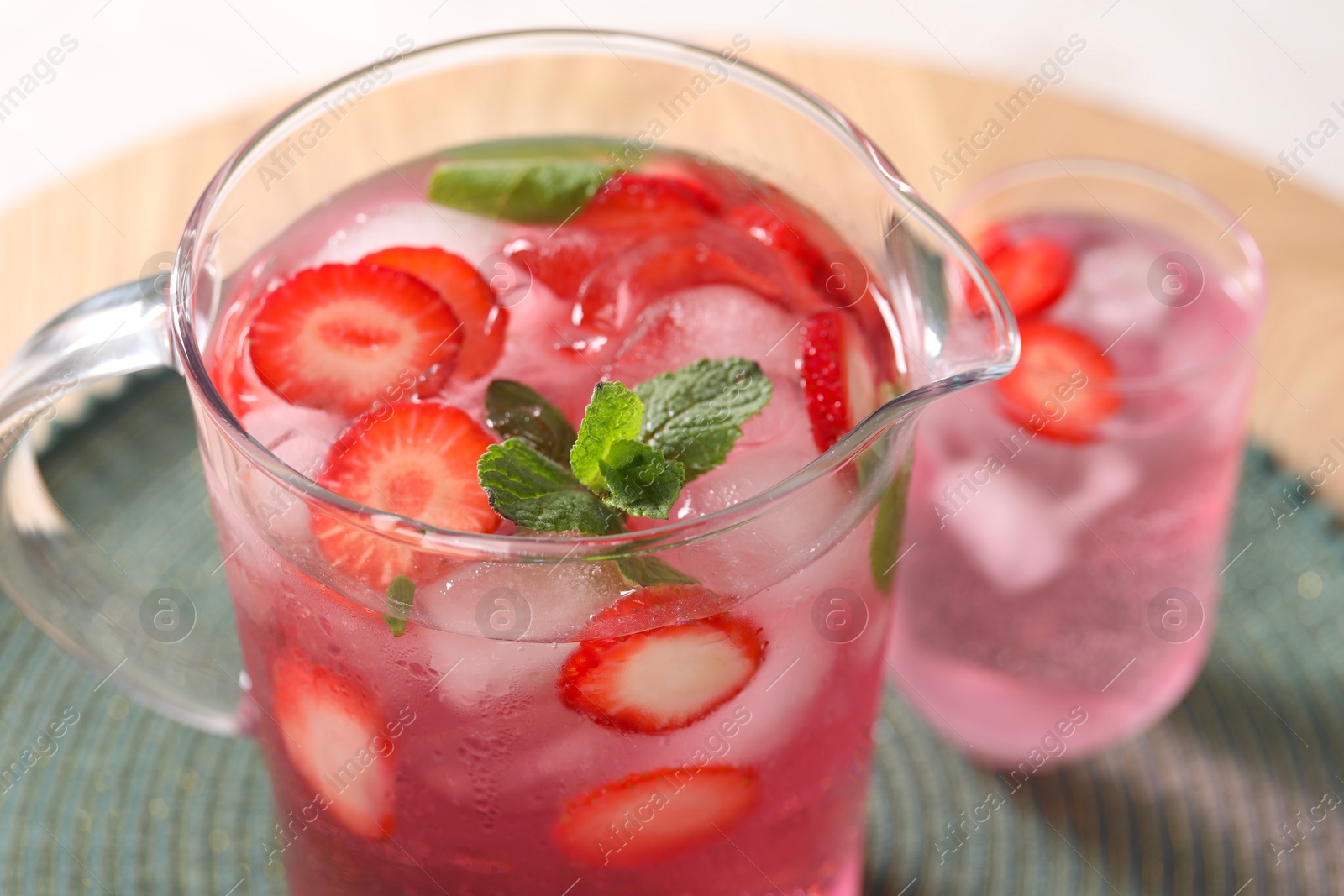 Photo of Freshly made strawberry lemonade with mint in jug and glass on wooden table, closeup