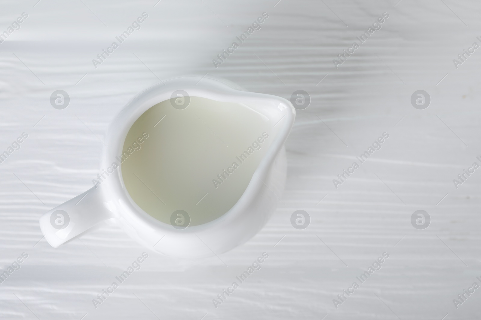 Photo of Jug of fresh milk on white wooden table, top view. Space for text