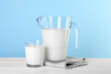 Jug and glass of fresh milk on white wooden table