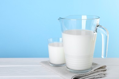 Photo of Jug and glass of fresh milk on white wooden table, space for text