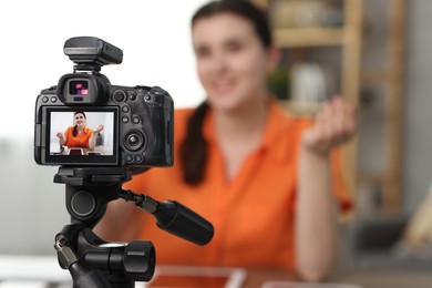 Photo of Technology blogger explaining something while recording video at home, focus on camera