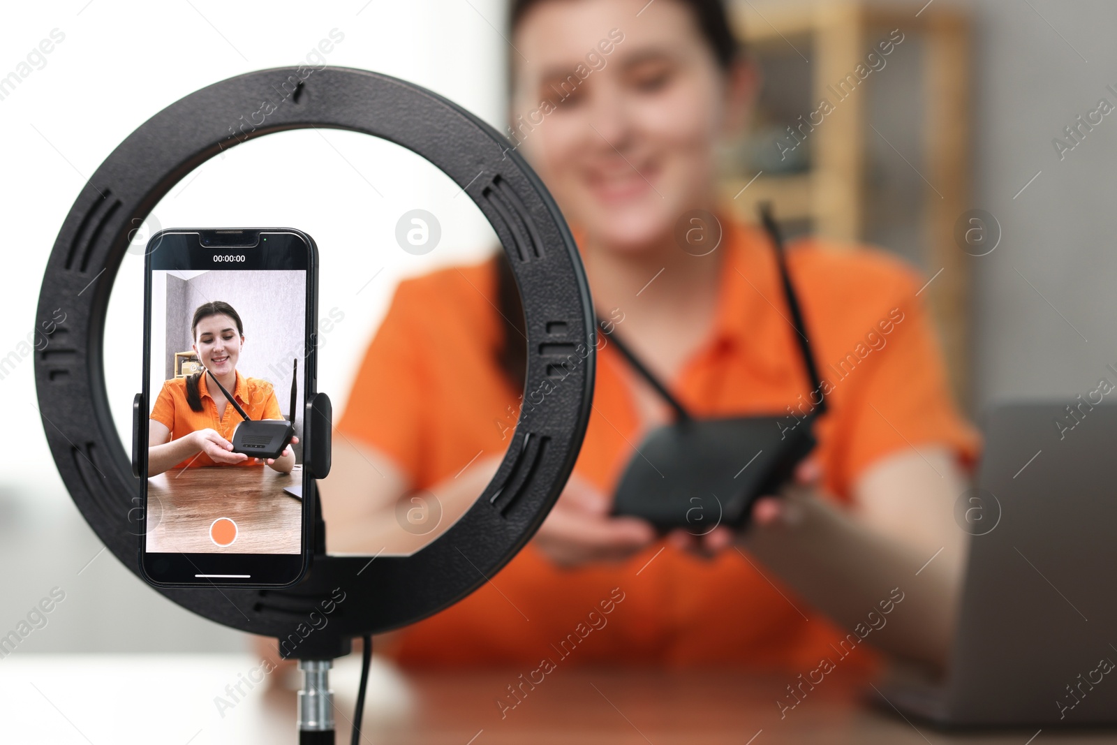 Photo of Technology blogger explaining something while recording video at home, focus on smartphone