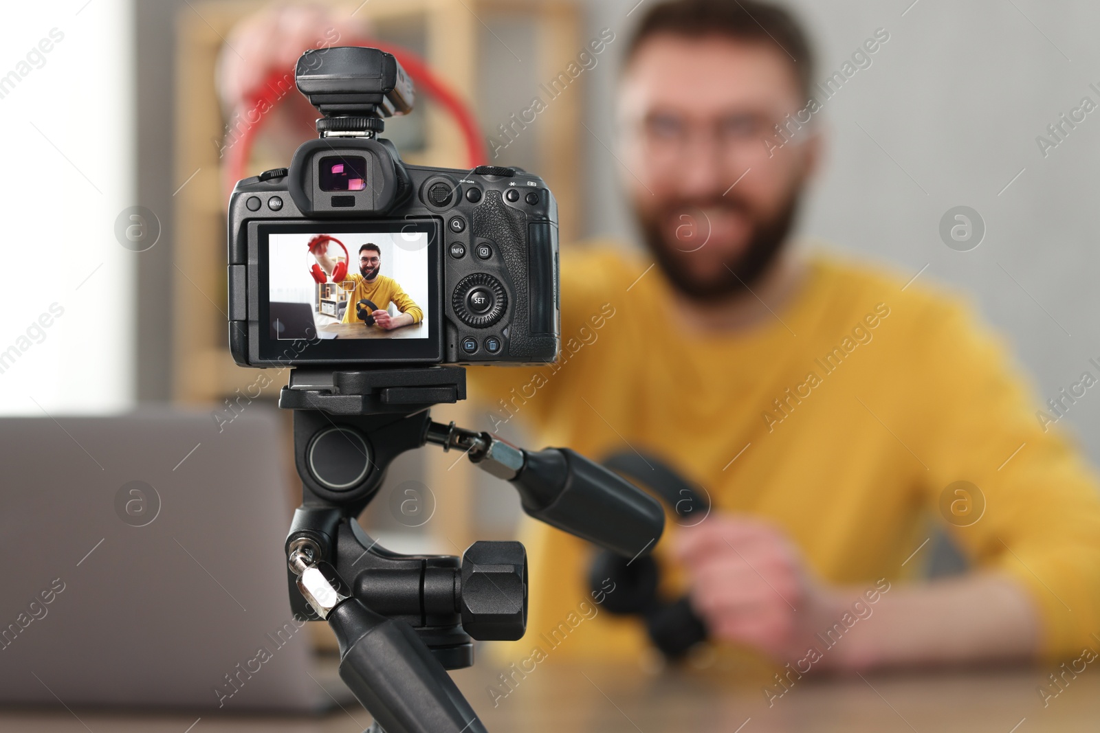 Photo of Technology blogger explaining something while recording video at home, focus on camera