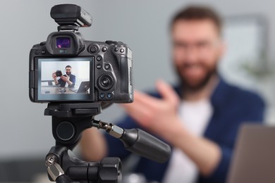 Photo of Technology blogger explaining something while recording video at home, focus on camera