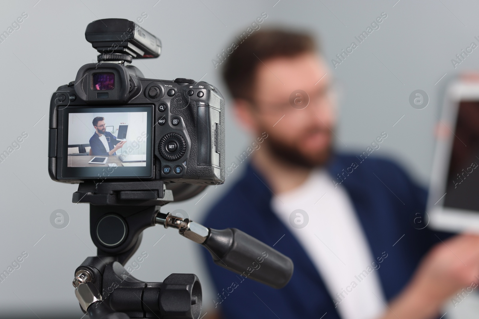 Photo of Technology blogger explaining something while recording video at home, focus on camera