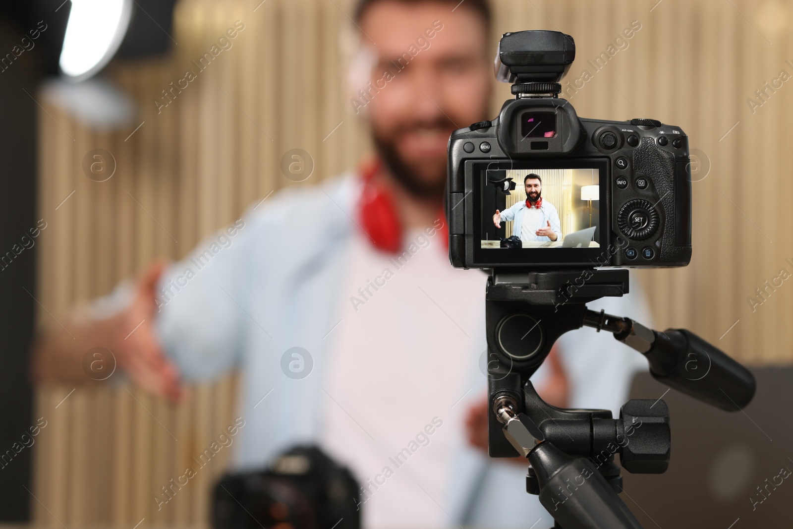 Photo of Technology blogger explaining something while recording video at home, focus on camera