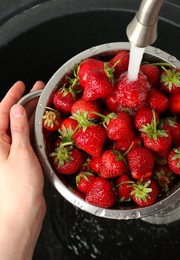 Photo of Woman washing fresh strawberries under tap water in metal colander above sink, top view