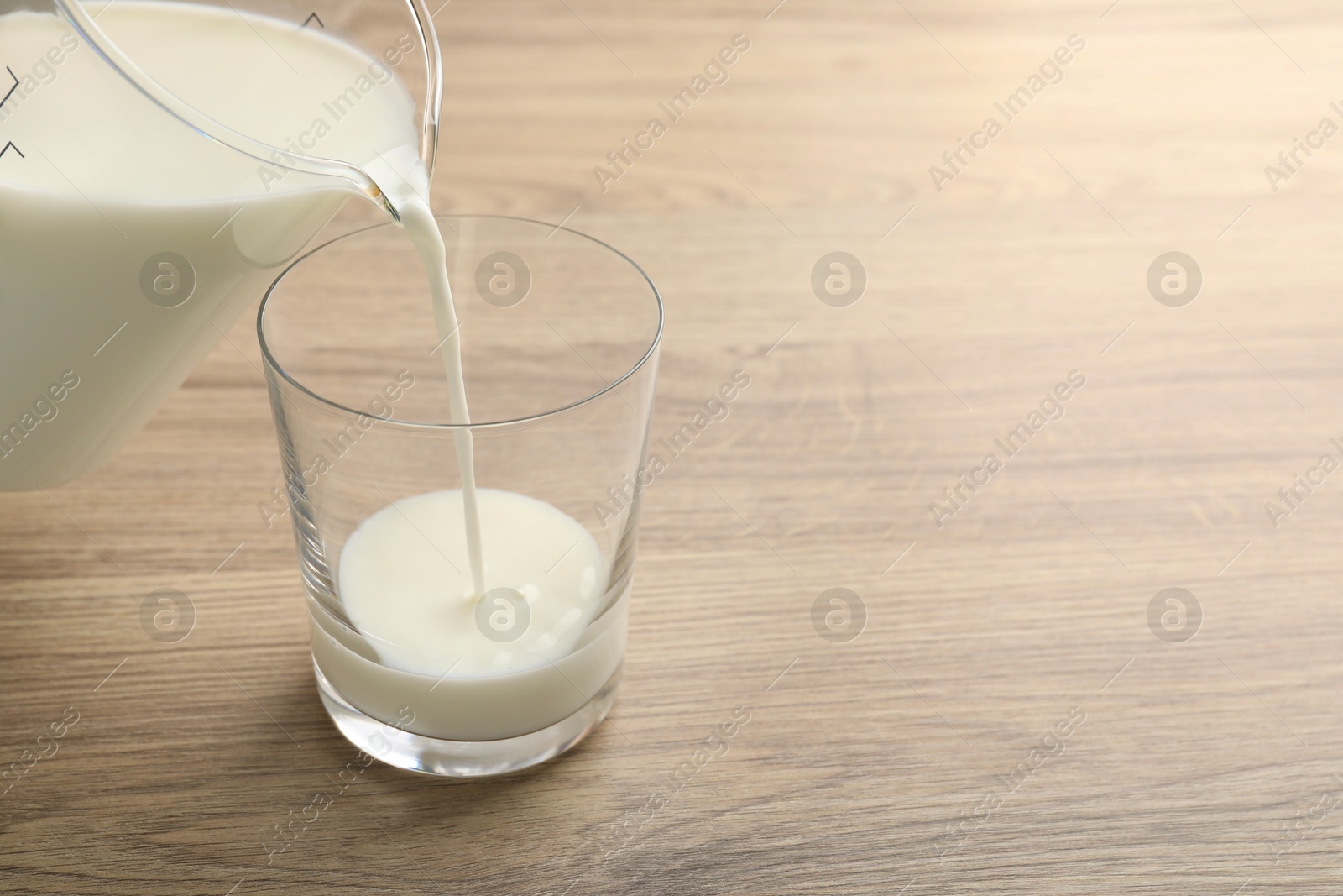 Photo of Pouring fresh milk from jug into glass at wooden table, closeup. Space for text