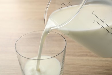 Photo of Pouring fresh milk from jug into glass at wooden table, closeup