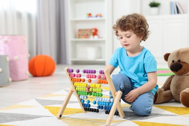 Cute little boy playing with wooden abacus on floor in kindergarten. Space for text