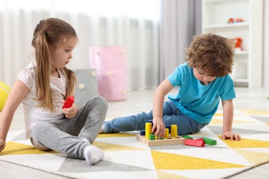 Photo of Cute little children playing with set of wooden geometric figures on floor in kindergarten