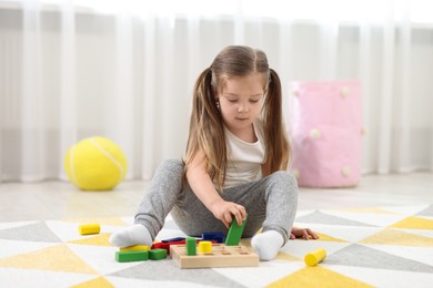 Cute little girl playing with set of wooden geometric figures on floor in kindergarten