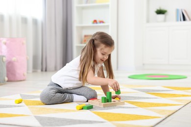 Photo of Cute little girl playing with set of wooden geometric figures on floor in kindergarten