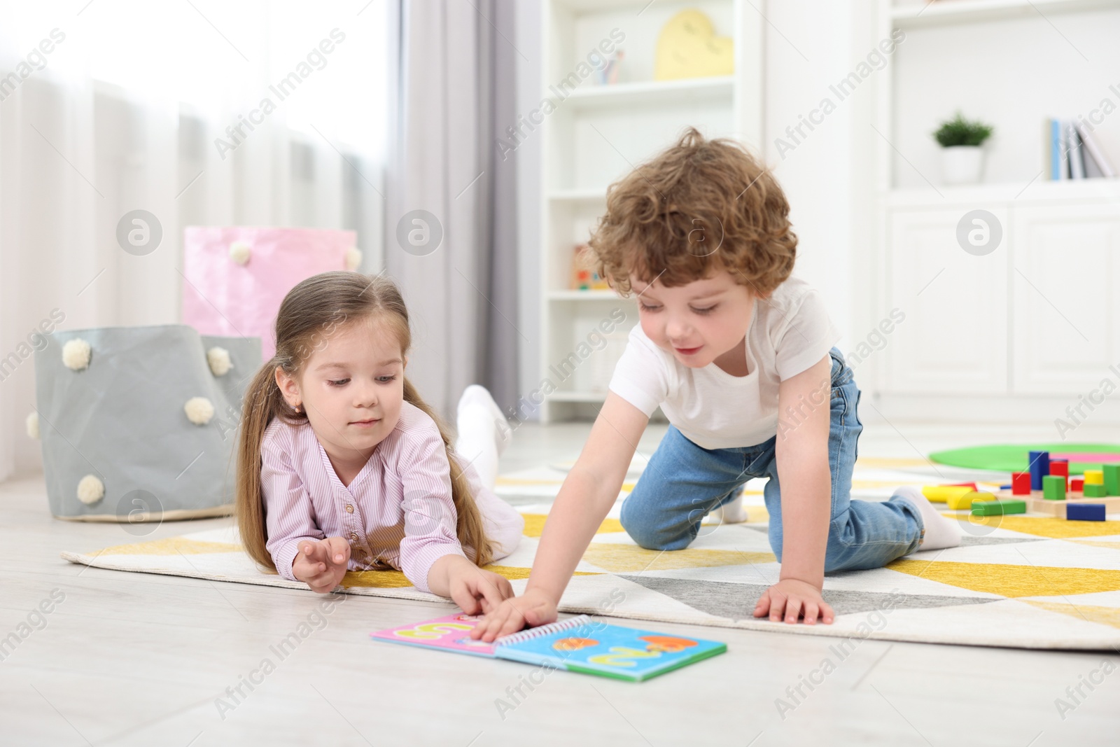 Photo of Cute little children reading book on floor in kindergarten