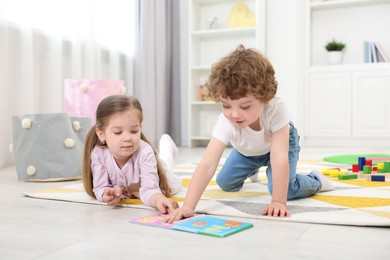 Cute little children reading book on floor in kindergarten