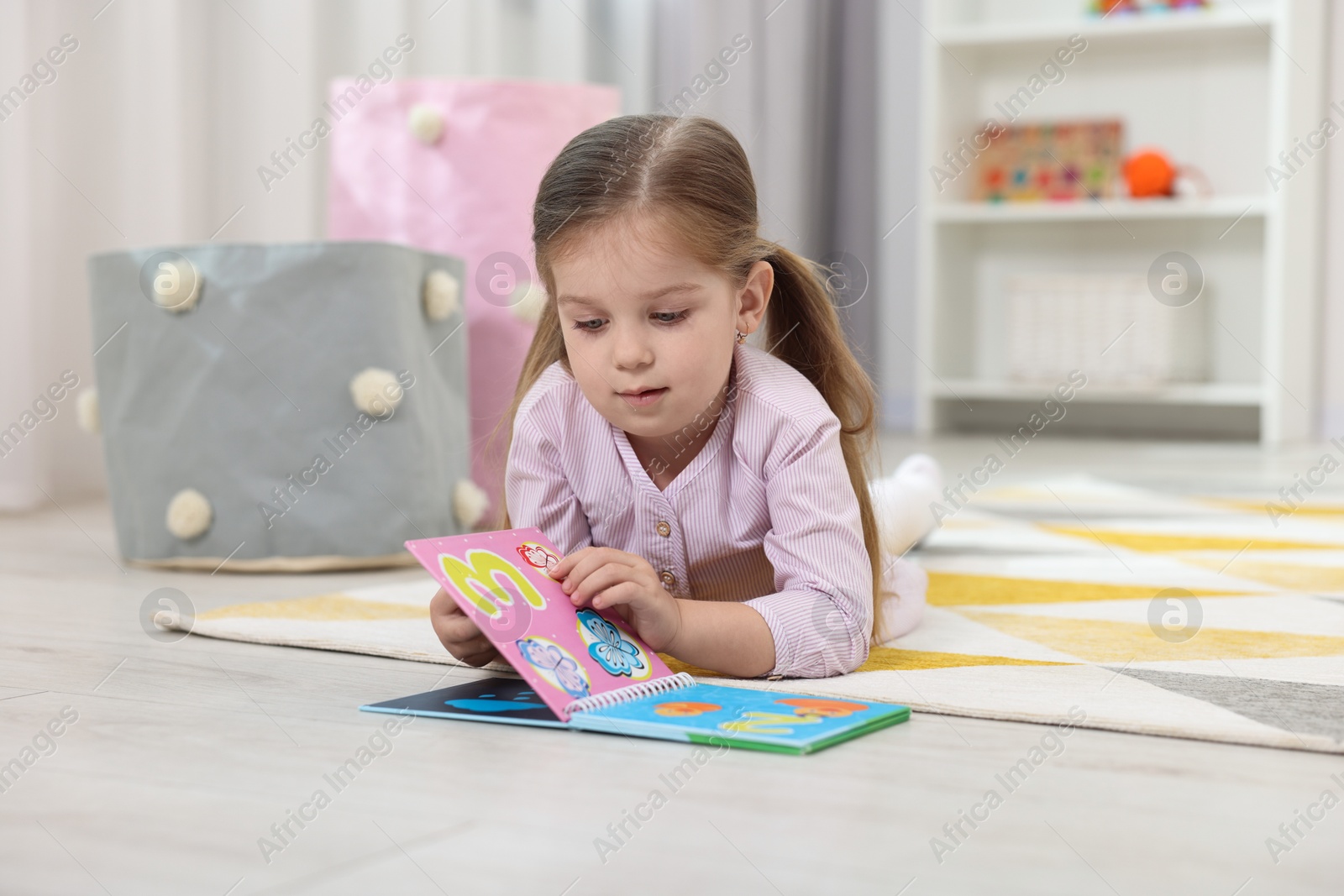 Photo of Cute little girl reading book on floor in kindergarten