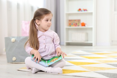 Cute little girl with book on floor in kindergarten. Space for text