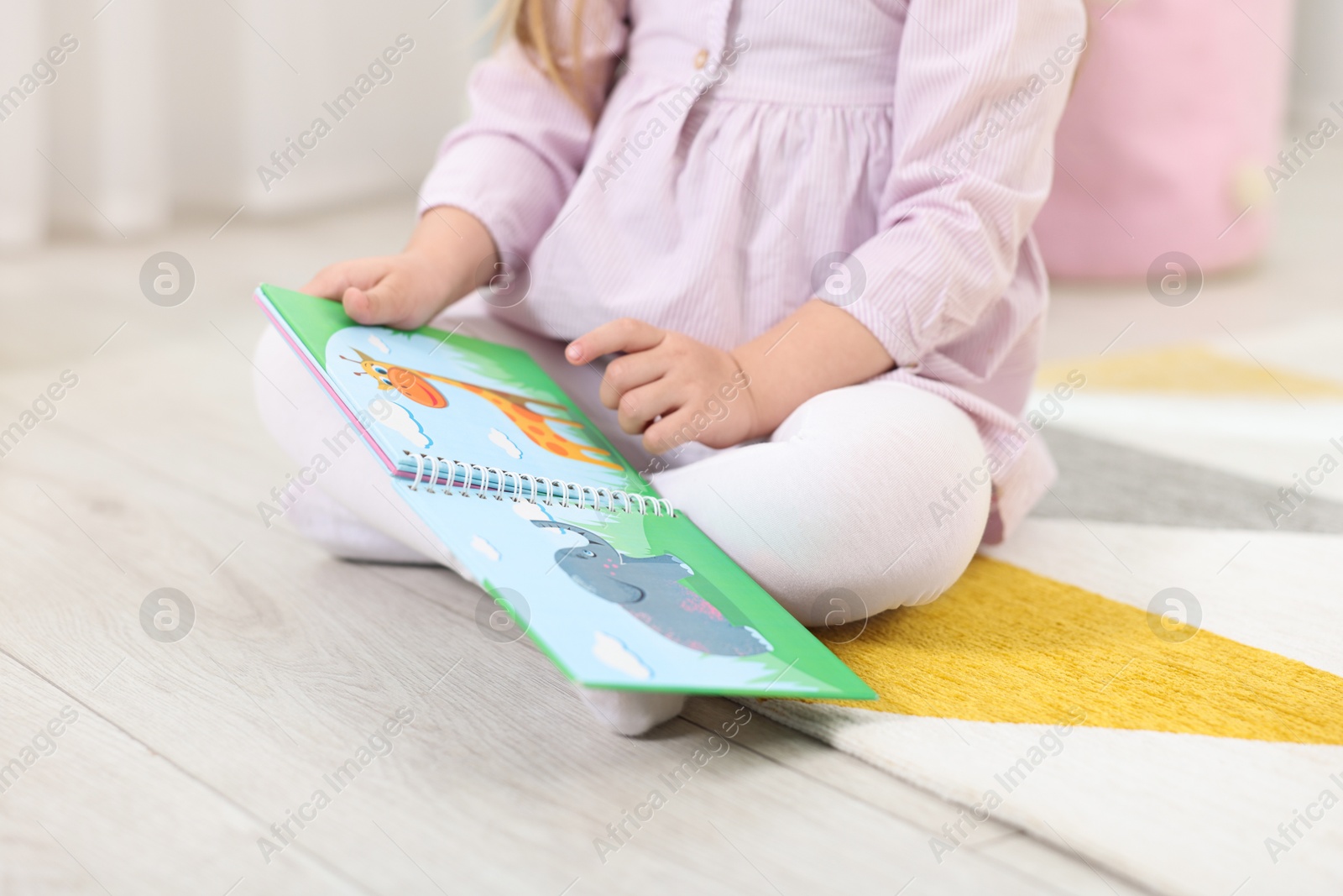 Photo of Little girl with book on floor in kindergarten, closeup