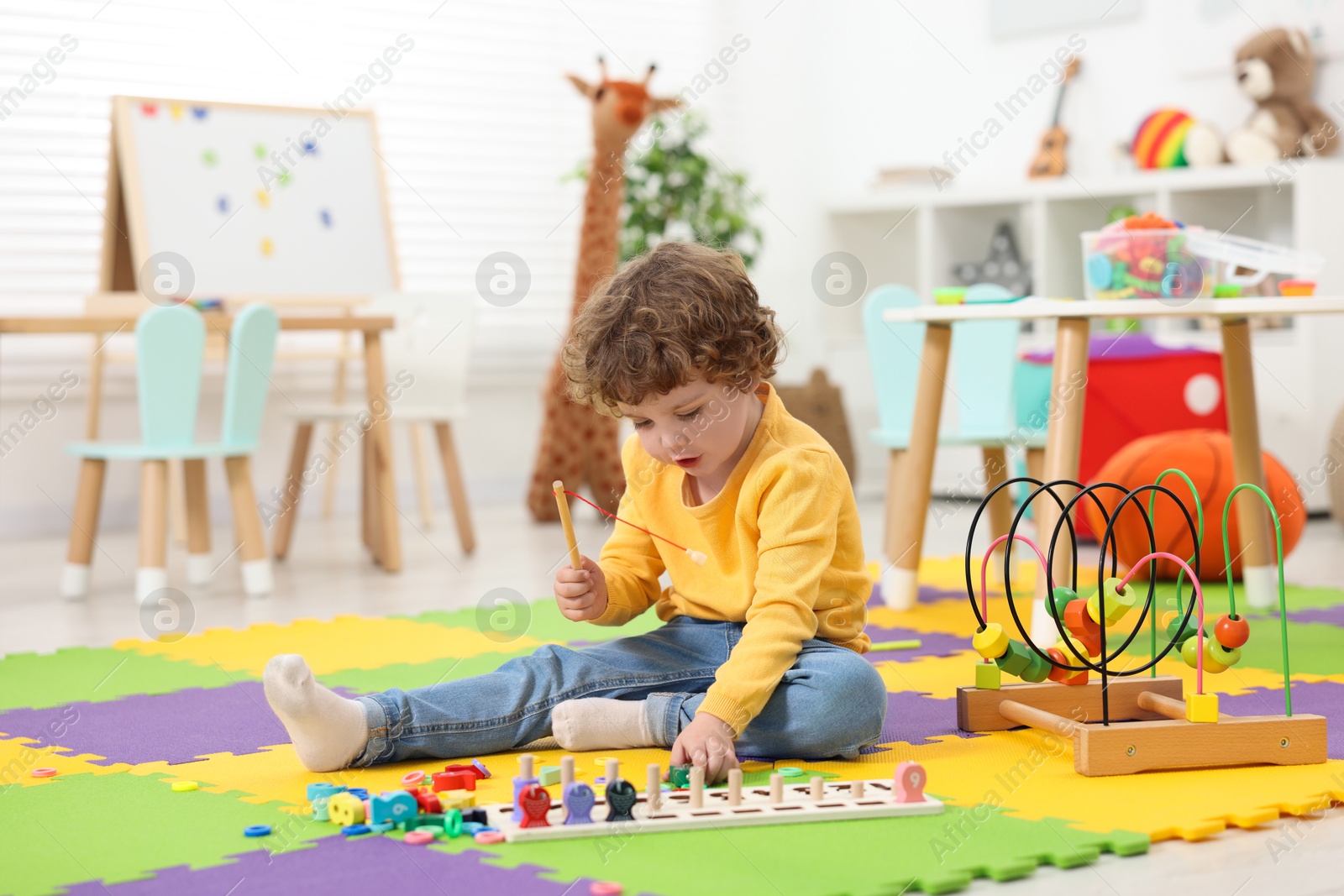 Photo of Cute little boy playing with math game Fishing for Numbers on puzzle mat in kindergarten