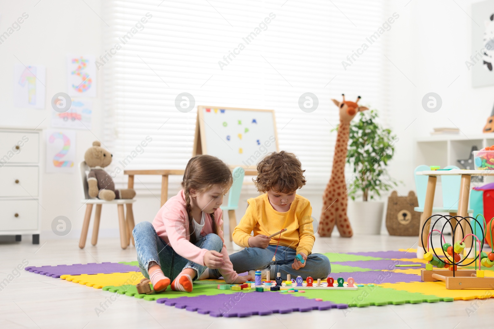 Photo of Cute little children playing with math game Fishing for Numbers on puzzle mat in kindergarten