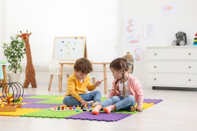 Cute little children playing with math game Fishing for Numbers on puzzle mat in kindergarten