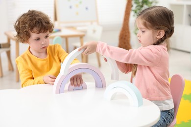 Photo of Cute little children playing with colorful toy rainbow at white table in kindergarten