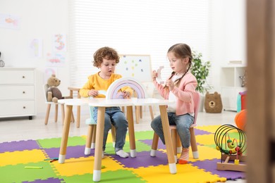 Cute little children playing with colorful toy rainbow at white table in kindergarten