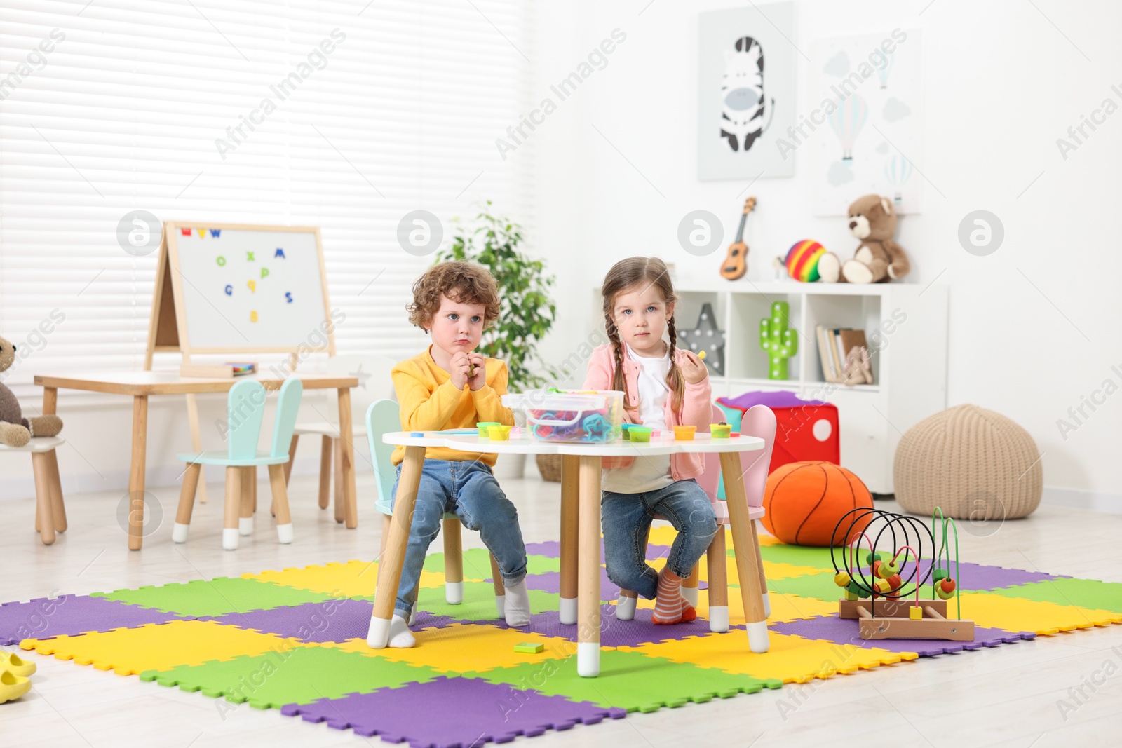 Photo of Cute little children modeling from plasticine at white table in kindergarten