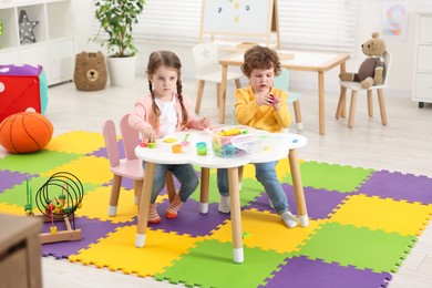Photo of Cute little children modeling from plasticine at white table in kindergarten
