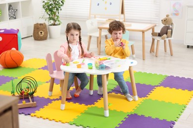 Cute little children modeling from plasticine at white table in kindergarten