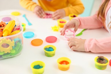 Photo of Little children modeling from plasticine at white table in kindergarten, closeup