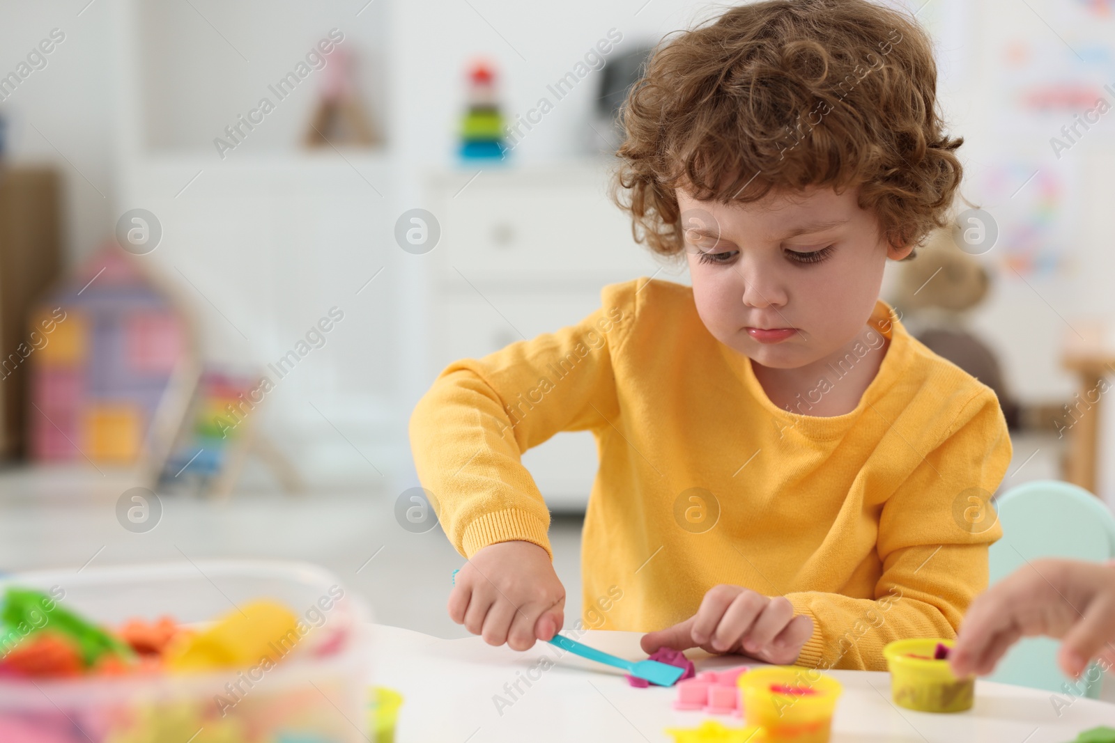 Photo of Cute little boy modeling from plasticine at white table in kindergarten. Space for text