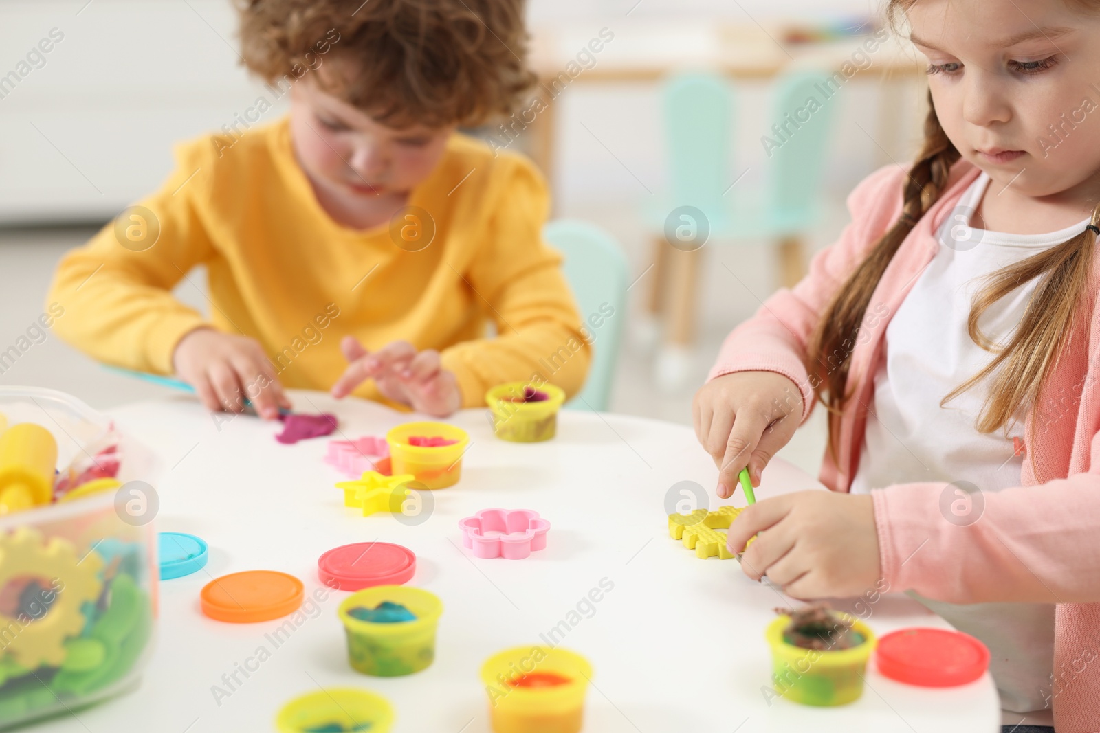 Photo of Little children modeling from plasticine at white table in kindergarten, closeup