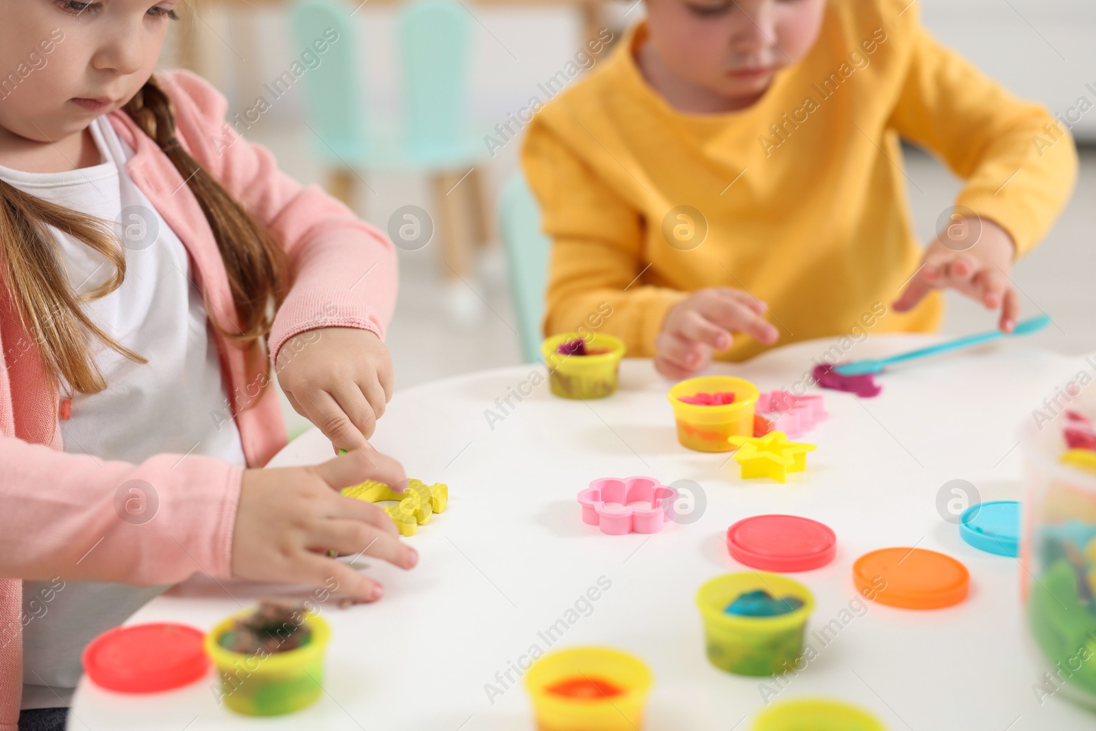 Photo of Little children modeling from plasticine at white table in kindergarten, closeup