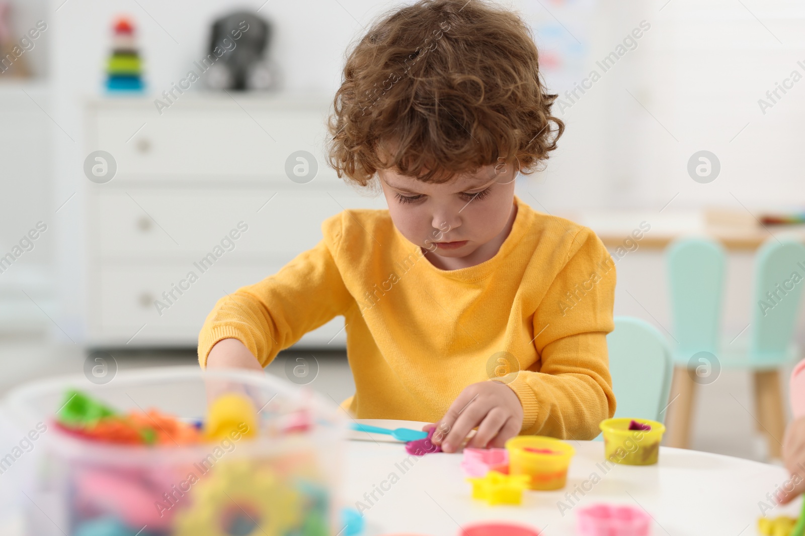 Photo of Cute little boy modeling from plasticine at white table in kindergarten