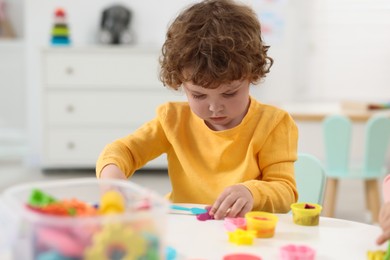 Cute little boy modeling from plasticine at white table in kindergarten