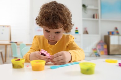 Cute little boy modeling from plasticine at white table in kindergarten