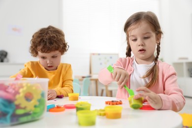 Cute little children modeling from plasticine at white table in kindergarten