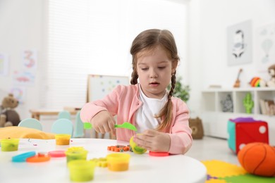 Cute little girl modeling from plasticine at white table in kindergarten