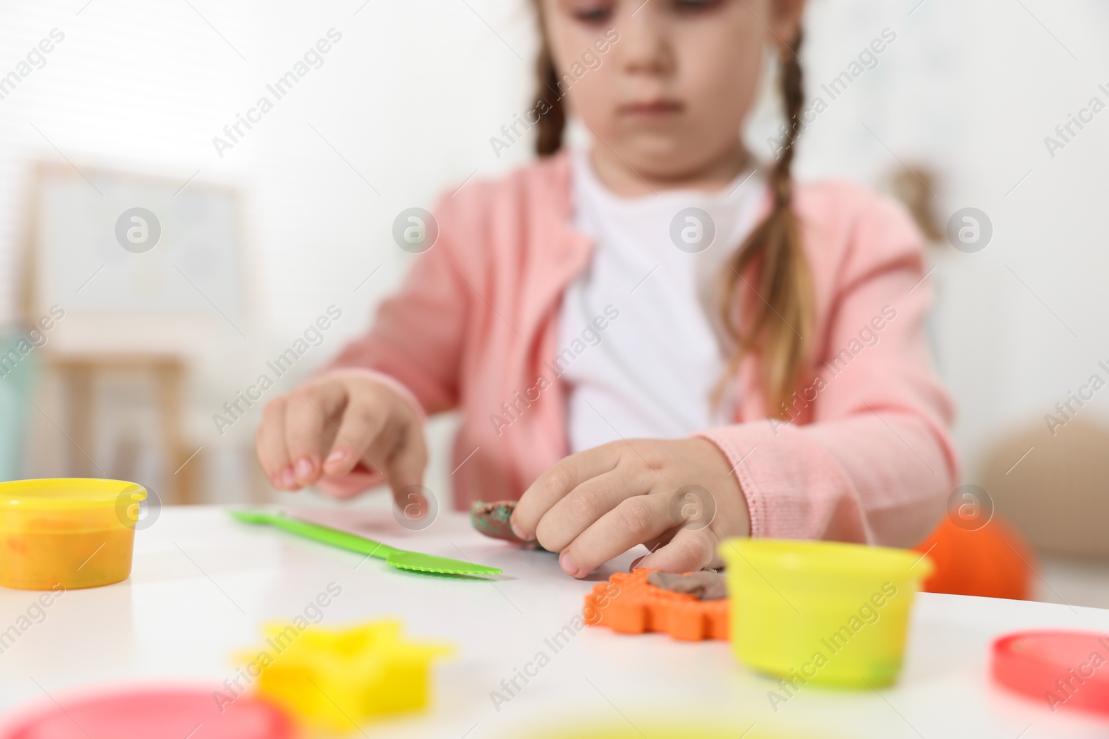 Photo of Little girl modeling from plasticine at white table in kindergarten, closeup