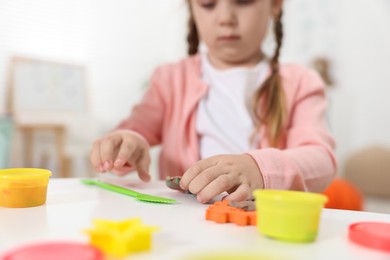 Little girl modeling from plasticine at white table in kindergarten, closeup