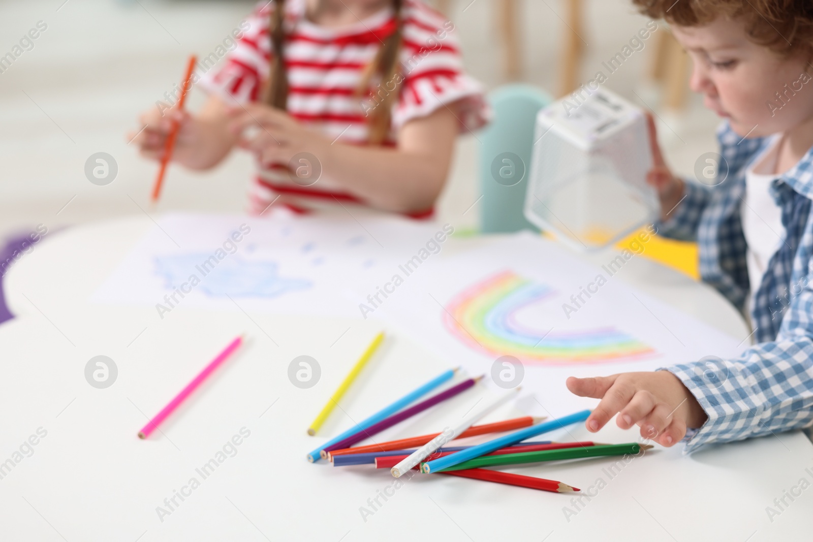 Photo of Little children drawing with colorful pencils at white table in kindergarten, closeup